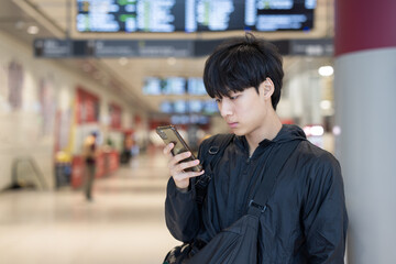 Fototapeta premium Young Man Using Smartphone at Bus Terminal Waiting Area