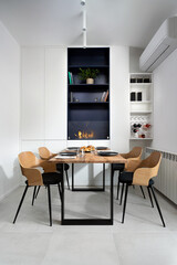 Bright modern dining room featuring a wooden table set for four, sculptural chairs, a built-in fireplace and shelving niche creating a cozy, minimalist atmosphere for meals and conversation.  © Manual Mood