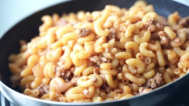 Hot macaroni stir-fried with minced meat in a pan, offering a delicious aroma and a comforting homemade meal