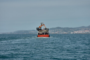 Fototapeta premium Traditional Galician mussel harvesting with an orange mussel boat off the coast of Vigo