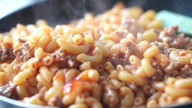 Hot macaroni stir-fried with minced meat in a pan, offering a delicious aroma and a comforting homemade meal
