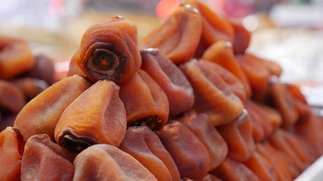 Pyramid stack of dried persimmons arranged carefully on a market selling surface with nearby retail counters forming a structured seasonal presentation. Seasonal food.