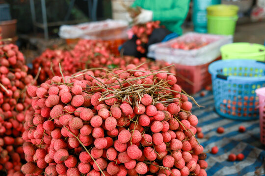 Fresh red lychee fruit heap on display for sale at vibrant outdoor tropical market. Abundance of delicious sweet fruit creates an inviting and authentic atmosphere