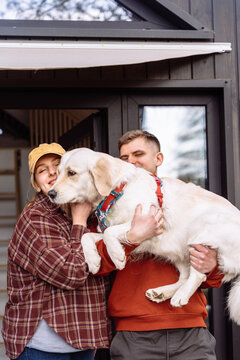 Young couple carrying golden retriever outside modern tiny house during countryside weekend escape