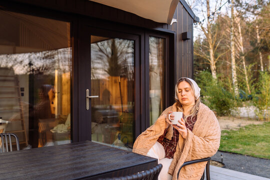Young woman drinking hot tea outside cozy tiny house during peaceful sunset retreat