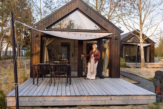 Woman opening modern Scandinavian tiny house terrace during calm golden hour evening