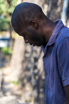 Thoughtful young Black man in quiet reflective moment outdoors in sunlight