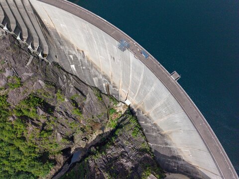 Aerial view of the Verzasca Dam showing its massive concrete wall curving between rocky cliffs and deep blue water in Gordola, Ticino, Switzerland.