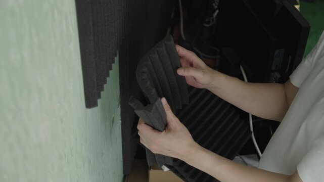 Sound engineer installing acoustic panels on wall for soundproofing and insulation in recording studio, improving room acoustics by reducing echo and reverberation, close-up, slow motion.