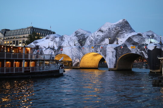 Paris, France - May 21, 2026. A view of the Seine River and the Pont-Neuf bridge at dusk with the JR installation on it. An art object which represent a mountain. 