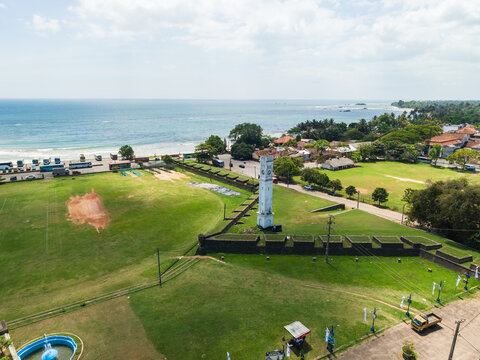 Aerial view of the historic Matara Fort clock tower and stone ramparts overlooking the blue ocean and coastline in Matara, Southern Province, Sri Lanka.