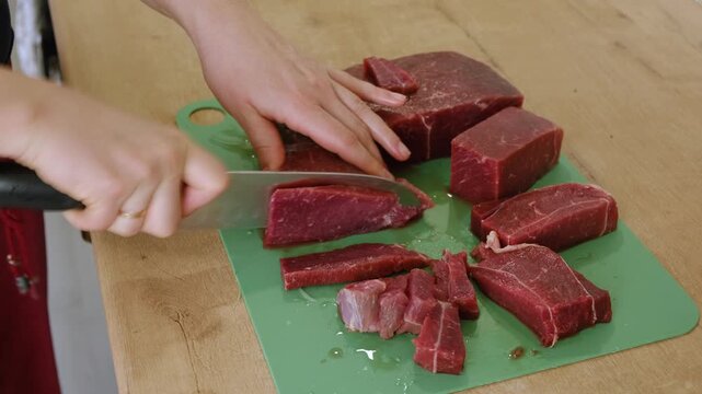 A housewife cuts beef on a cutting board. Close-up of hands with a knife cutting meat. Healthy eating. Preparing a raw beef steak for a family dinner. Handling raw meat. Cooking. Homemade food.