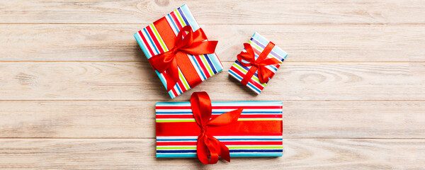 Fototapeta premium Beautiful gift box with a colored bow on the yellow wooden table. Top view banner with copy space for you design