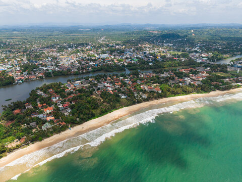 Aerial view of the coastal town with sandy beaches, turquoise ocean waves, and the Nilwala River flowing through lush greenery Matara, Southern Province, Sri Lanka.