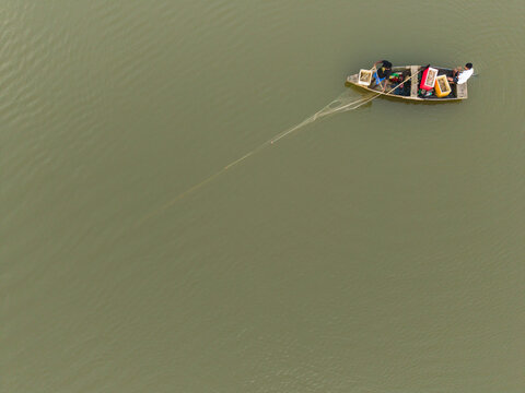 Aerial view of two fishermen in a small wooden boat pulling a fishing net on calm murky water in Galle, Southern Province, Sri Lanka.