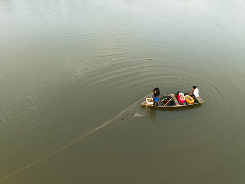 Aerial view of fishermen in a small wooden boat pulling a fishing net on calm water in Galle, Southern Province, Sri Lanka.