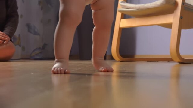 Baby feet take first uncertain wobbly steps on a wooden floor. Early childhood development and learning to walk