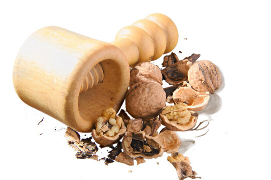Handheld wooden nutcracker surrounded by cracked walnuts and scattered shells on white background, evoking rustic kitchen prep, natural ingredients and wholesome healthy snacking or baking use.