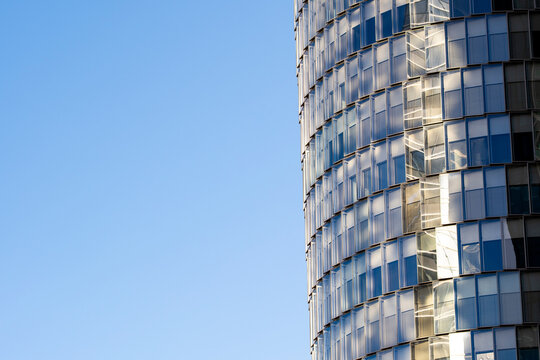 Glass tower architecture cuts into blue sky above a reflective facade, leaving urban building negative space across a clean vertical edge