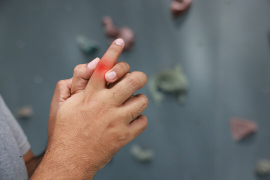 Close up of an unrecognizable man suffering from finger joint pain with glowing red graphic overlay after rock climbing. Sports injury, arthritis and healthcare concept.