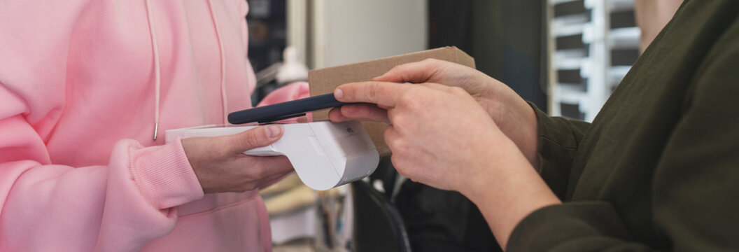 Woman paying with card for parcel delivery for courier. Electronic cashless payments. Online shopping. A woman enters a PIN code on a wireless payment terminal. nfc payment banner