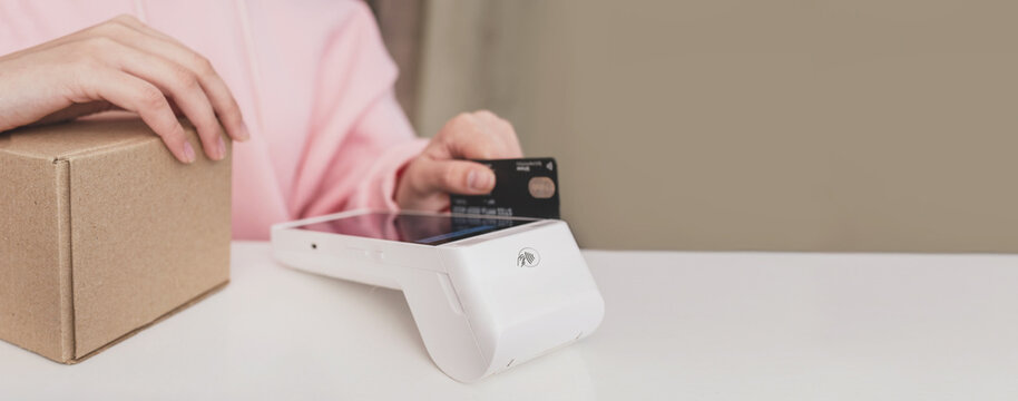 Paying with a magnetic stripe card for parcel delivery. Electronic cashless payments. Online shopping. A woman enters a PIN code on a wireless payment terminal.