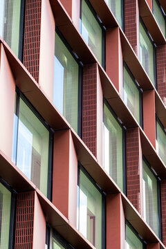 Red facade architecture repeats window frames and shadow across an urban building, where geometric pattern and texture rise in vertical light