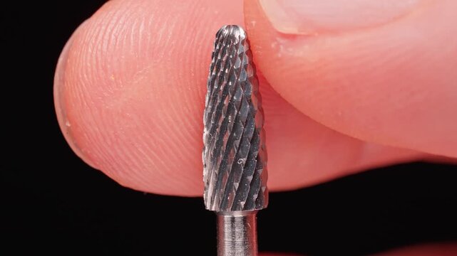 Professional Carbide Manicure Drill Bit Held Between Fingers, Extreme Macro Closeup of Nail Milling Cutter Texture, Precision Beauty Tool for Hardware Nail Care and Salon Work