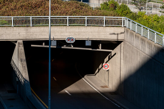 A concrete underpass in Oslo carries road traffic beneath a bridge, with urban transport infrastructure, a sign and deep shadow shaping the entrance