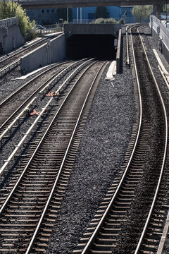 Railway tracks in Oslo curve toward a tunnel, where urban transport infrastructure forms parallel lines over gravel and shadowed depth
