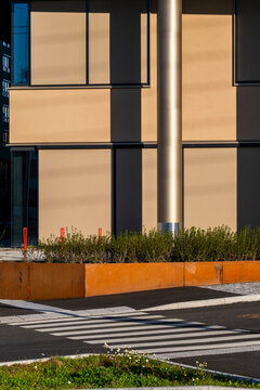 Sunlight cuts across an Oslo building facade beside a crosswalk, where urban street columns and planter edges frame a sharp corner