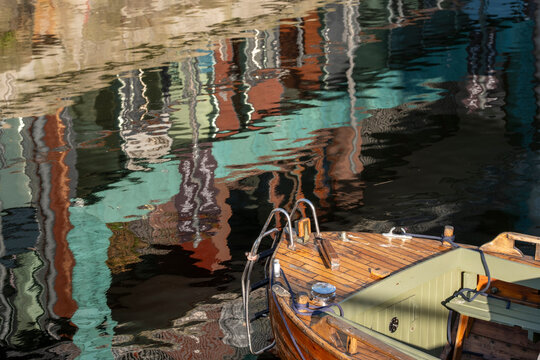A small boat rests in Oslo harbor water beside rippled reflections, where urban colors and quay details shape an abstract waterfront view