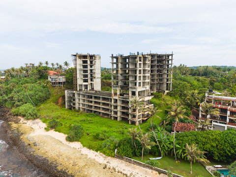 Aerial view of an unfinished concrete building skeleton on a lush tropical coastline with palm trees and ocean waves Mirissa, Southern Province, Sri Lanka.