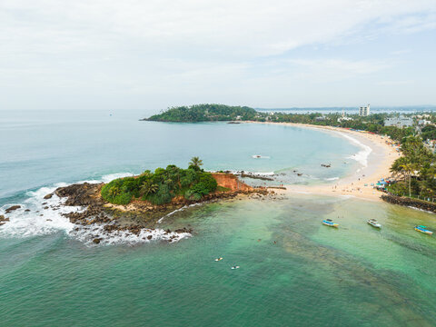 Aerial view of Parrot Rock and the sandy coastline with turquoise waters and palm trees in Mirissa, Southern Province, Sri Lanka.