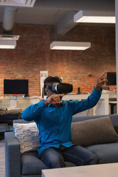 Man wearing VR headset is reaching and pointing on gray-blue sofa in office lounge