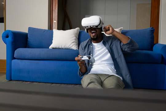 African American man in his 20s playing VR game in front of blue sofa, holding controller