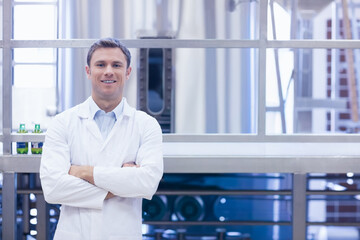 Fototapeta premium Adult man wearing white lab coat inspecting stainless-steel tanks and green glass bottles at plant