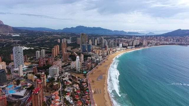 Panoramic view of Benidorm, Spain, showcasing the curved sandy beach, turquoise Mediterranean sea, high-rise buildings and mountain backdrop