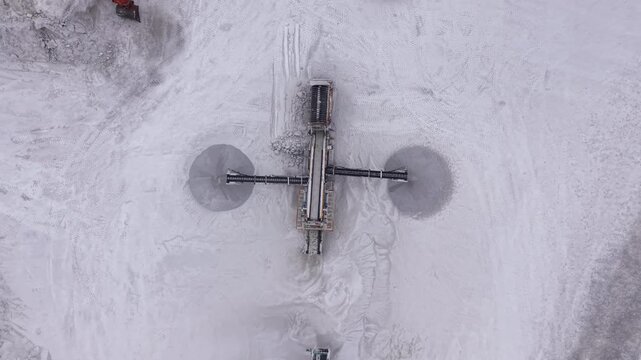Top-down view of a mobile screener operating in a white gypsum quarry, sorting mineral material with conveyor belts extending outward, excavator visible nearby
