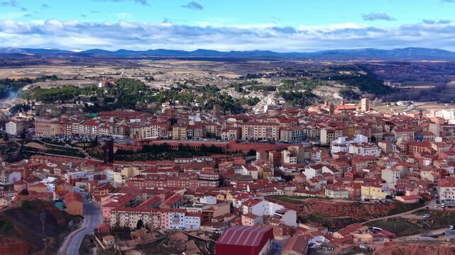 Panoramic view of Teruel, Spain, showing terracotta rooftops, historic buildings, surrounding valleys and mountains under a partly cloudy sky