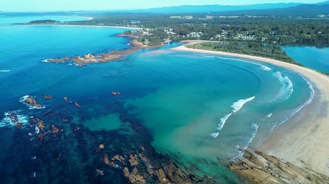 Drone aerial landscape of ocean waves crashing along the rocky shoreline at Tomakin Beach with Mossy Point headland and the Tomaga River in the background South Coast NSW Australia tourism and nature