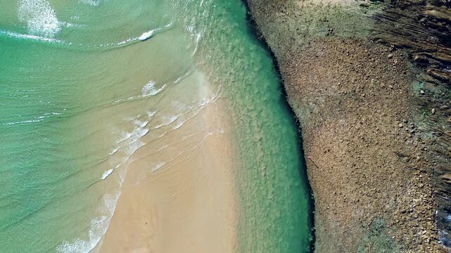Drone aerial landscape of clear ocean waves crashing on beach sandbar intersecting with Tomaga River inlet beside rocky headland at Mossy Point town suburbs on the South Coast NSW Australian tourism
