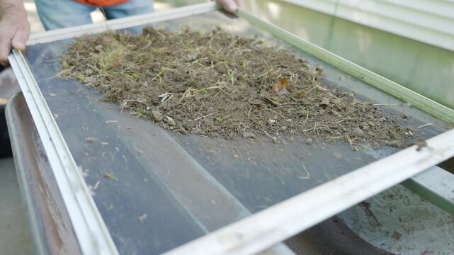 Male hands sifting soil and compost through a screen sieve to remove debris for gardening