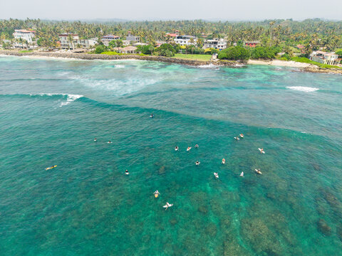 Aerial view of surfers waiting for waves in clear turquoise water near the coastline of Devil's Rock, Ahangama, Southern Province, Sri Lanka.