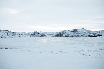 Horizontal shot of frozen lake surrounded by snow covered mountains in Teriberka, winter arctic tundra landscape, cold northern nature wilderness background, polar day white scenic view © Krystsina