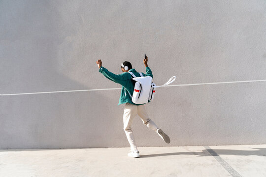 Man with backpack and headphones dancing on footpath