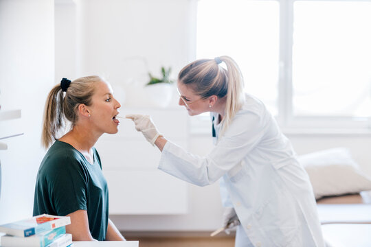 Female doctor examining female patient with tongue depressor