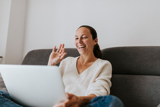Happy woman waving hand video call on laptop at home