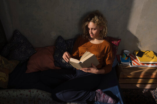Blond student sitting on bed reading a book