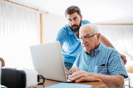 Adult grandson teaching his grandfather to use laptop